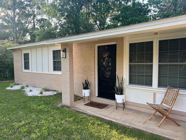 property entrance with a lawn, board and batten siding, and brick siding