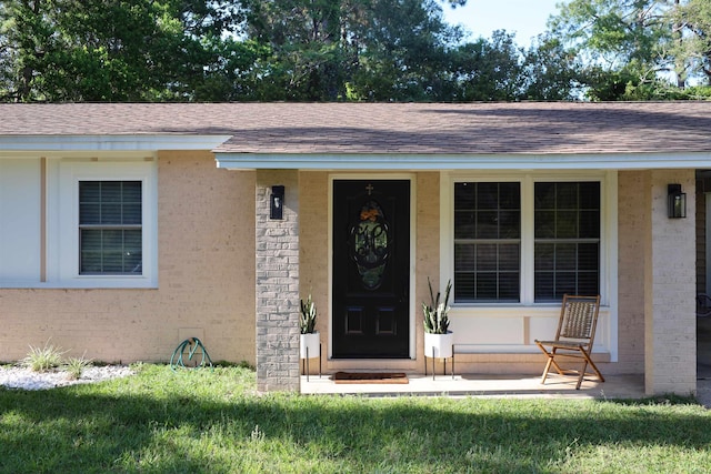 entrance to property with covered porch, a shingled roof, and brick siding