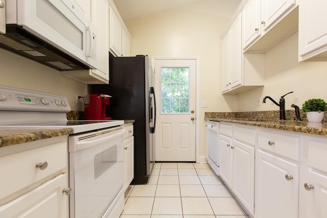 kitchen featuring white appliances, dark stone counters, sink, light tile patterned flooring, and white cabinetry