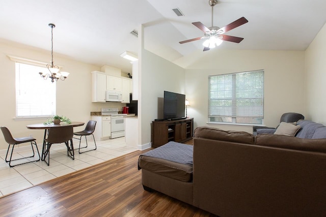 living room with ceiling fan with notable chandelier, lofted ceiling, and light wood-type flooring