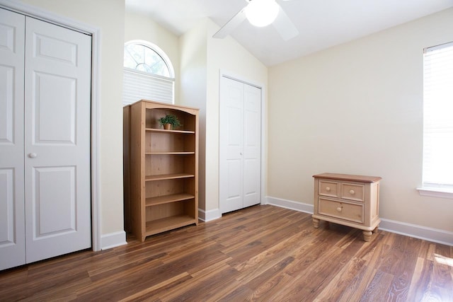 unfurnished bedroom with two closets, ceiling fan, dark wood-type flooring, and lofted ceiling