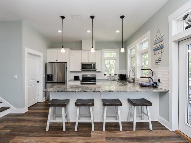 kitchen with white cabinets, light stone counters, appliances with stainless steel finishes, decorative light fixtures, and a sink