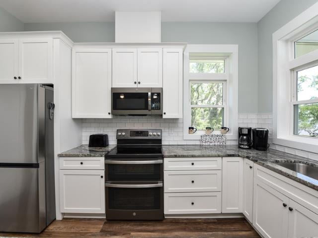 kitchen featuring appliances with stainless steel finishes, a wealth of natural light, white cabinetry, and dark stone countertops