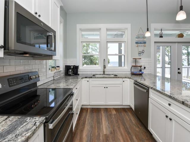 kitchen with white cabinets, light stone counters, hanging light fixtures, stainless steel appliances, and a sink