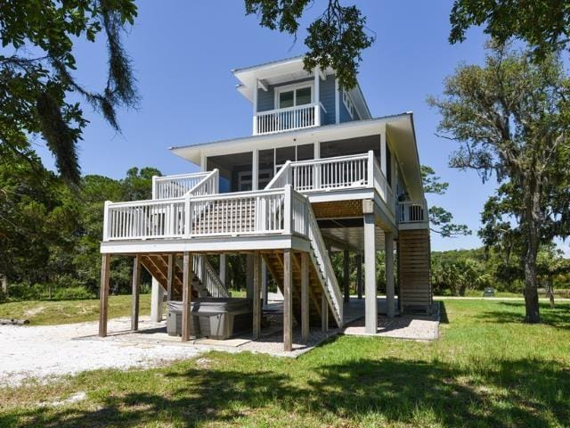 rear view of house with a sunroom, a hot tub, and a yard