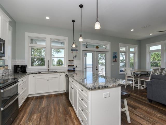 kitchen with pendant lighting, appliances with stainless steel finishes, white cabinets, a sink, and light stone countertops