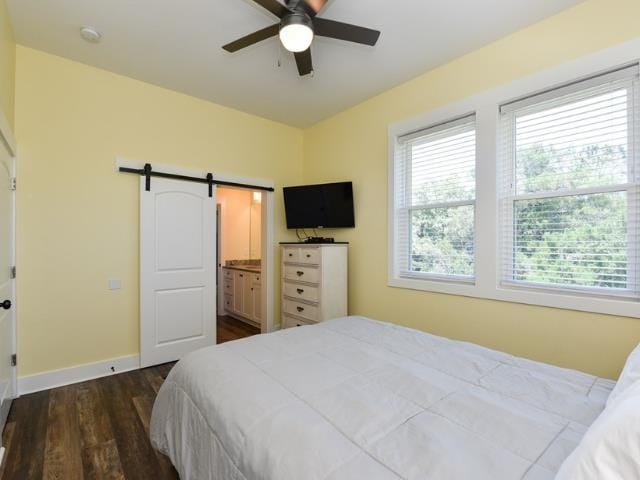 bedroom with a barn door, multiple windows, baseboards, and dark wood-style flooring