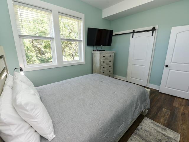 bedroom with a barn door, dark wood-type flooring, and baseboards