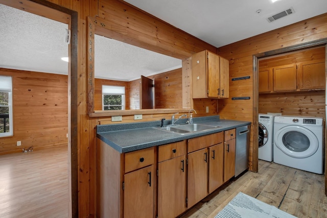 kitchen featuring stainless steel dishwasher, wooden walls, washer and clothes dryer, and sink