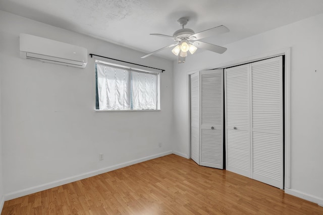 unfurnished bedroom with ceiling fan, a wall mounted AC, a closet, and light hardwood / wood-style flooring