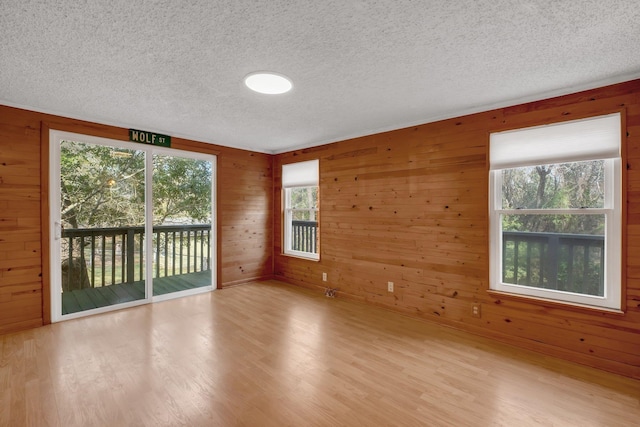 empty room with light wood-type flooring, a textured ceiling, and wood walls