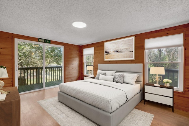 bedroom with a textured ceiling, access to exterior, light wood-type flooring, and wood walls