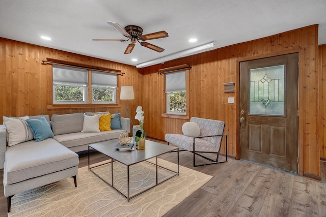 living room with wooden walls, ceiling fan, and light hardwood / wood-style flooring