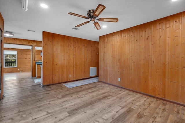 spare room with ceiling fan, wooden walls, and light wood-type flooring