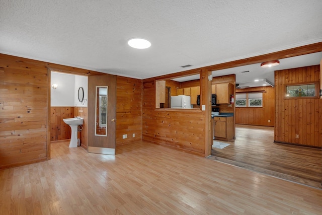 interior space with sink, light hardwood / wood-style flooring, wood walls, and white fridge