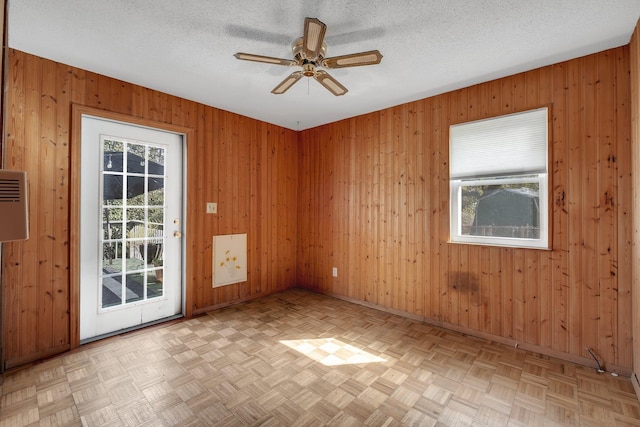 unfurnished room featuring light parquet floors, ceiling fan, a textured ceiling, and wood walls