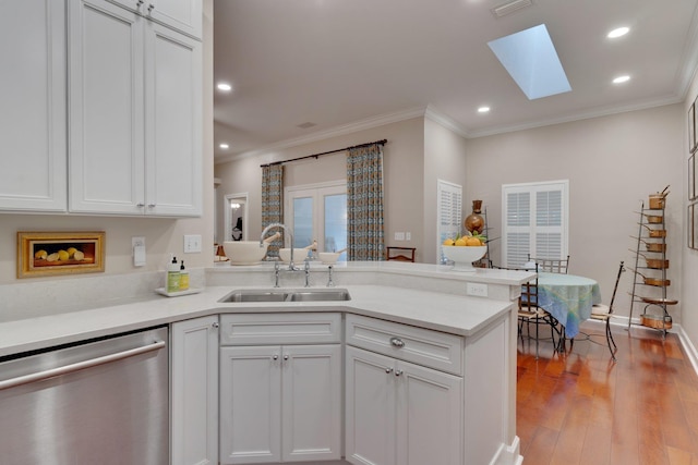 kitchen with a skylight, white cabinetry, sink, stainless steel dishwasher, and kitchen peninsula