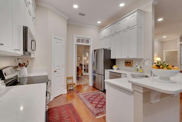 kitchen with sink, stainless steel appliances, white cabinets, a kitchen bar, and kitchen peninsula