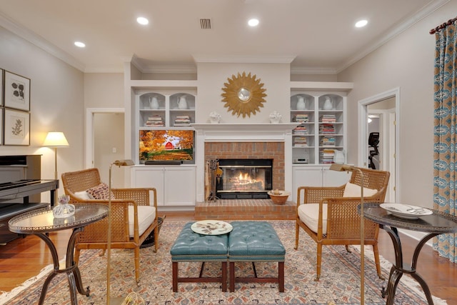 living room with crown molding, built in shelves, a fireplace, and light hardwood / wood-style floors