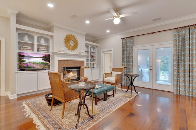 sitting room with built in shelves, ceiling fan, wood-type flooring, and french doors