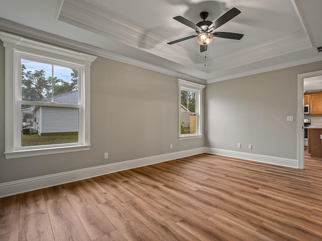 empty room with ceiling fan, ornamental molding, light hardwood / wood-style flooring, and a raised ceiling