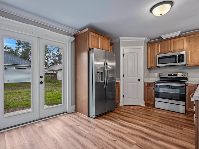 kitchen with a wealth of natural light, appliances with stainless steel finishes, crown molding, and light wood-type flooring