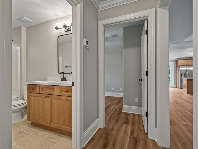 bathroom with toilet, vanity, wood-type flooring, and crown molding