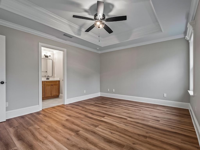 unfurnished bedroom featuring ceiling fan, hardwood / wood-style floors, ensuite bath, a tray ceiling, and ornamental molding