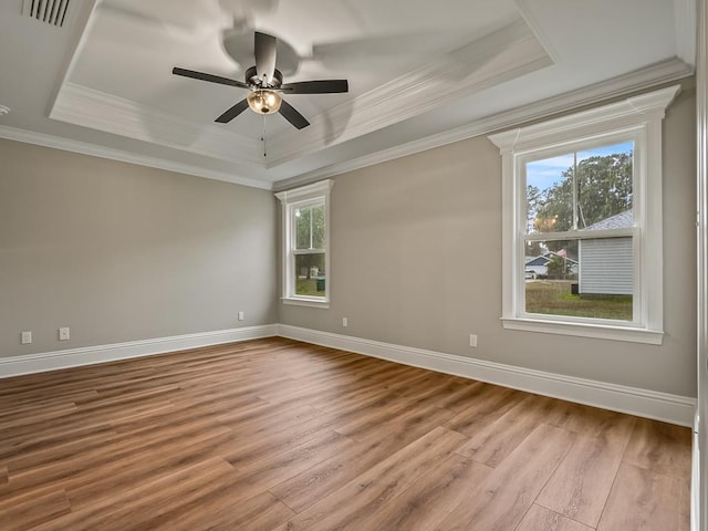 unfurnished room featuring a raised ceiling, ceiling fan, light wood-type flooring, and crown molding