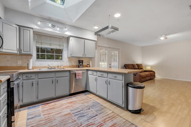 kitchen with gray cabinets, light wood-type flooring, tasteful backsplash, kitchen peninsula, and stainless steel appliances