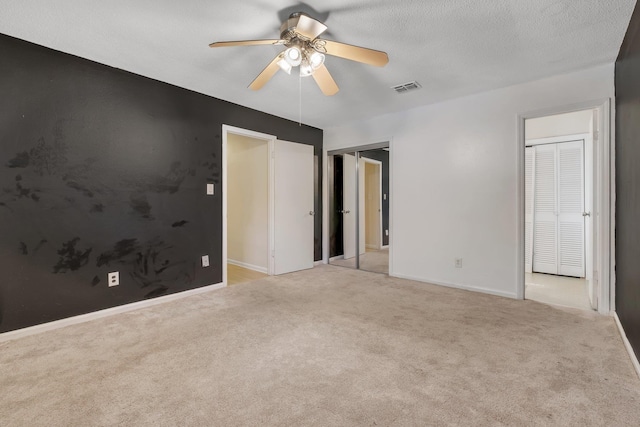 unfurnished bedroom featuring light carpet, a textured ceiling, and ceiling fan