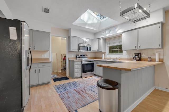 kitchen featuring appliances with stainless steel finishes, gray cabinets, a skylight, and light hardwood / wood-style flooring