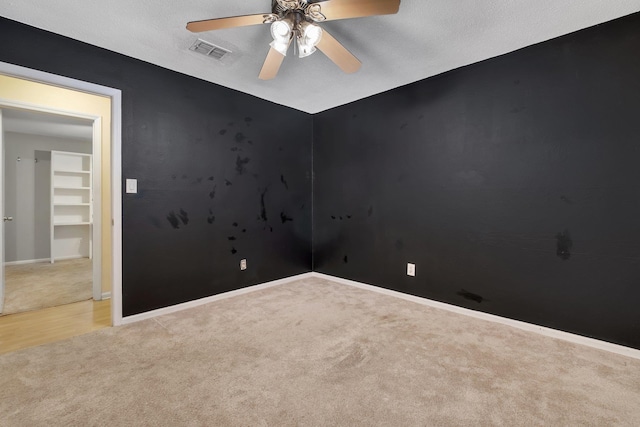 empty room with ceiling fan, light colored carpet, and a textured ceiling