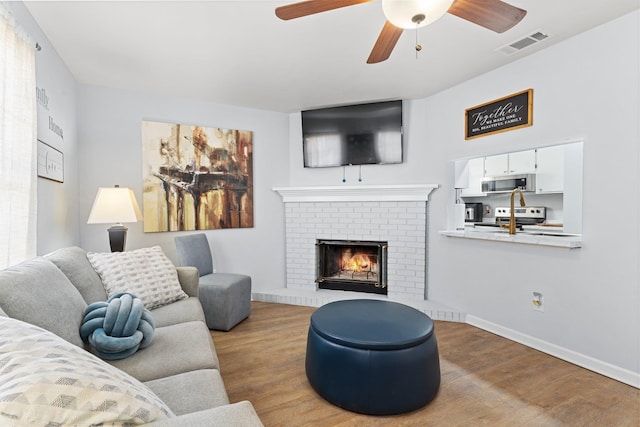 living room with a fireplace, ceiling fan, and light hardwood / wood-style flooring