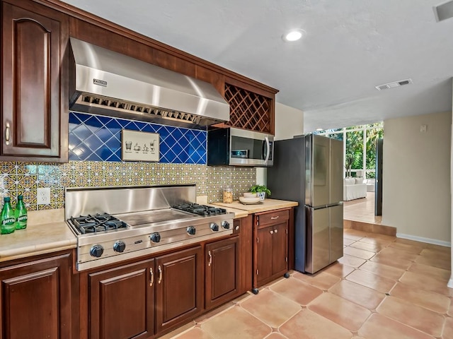 kitchen featuring appliances with stainless steel finishes, tasteful backsplash, light tile patterned floors, and wall chimney range hood