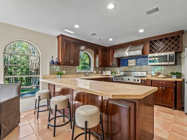 kitchen featuring backsplash, kitchen peninsula, wall chimney range hood, and stainless steel appliances