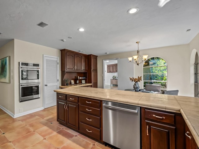 kitchen with appliances with stainless steel finishes, dark brown cabinetry, a notable chandelier, hanging light fixtures, and tile counters