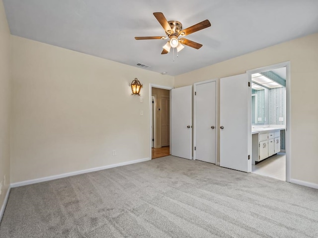 unfurnished bedroom with a closet, light colored carpet, ensuite bath, and ceiling fan