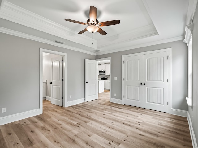 unfurnished bedroom with a raised ceiling, light hardwood / wood-style flooring, ceiling fan, ornamental molding, and a closet