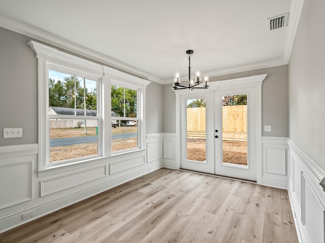 unfurnished dining area with a notable chandelier, ornamental molding, french doors, and light hardwood / wood-style flooring