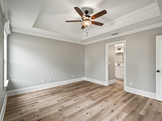 unfurnished bedroom with a tray ceiling, ensuite bath, ceiling fan, and crown molding