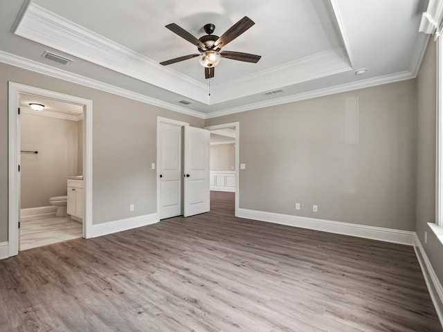 unfurnished bedroom featuring connected bathroom, ceiling fan, a raised ceiling, crown molding, and light hardwood / wood-style floors