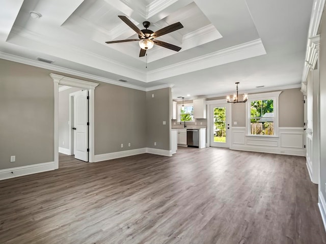 unfurnished living room with ceiling fan with notable chandelier, a raised ceiling, wood-type flooring, and crown molding