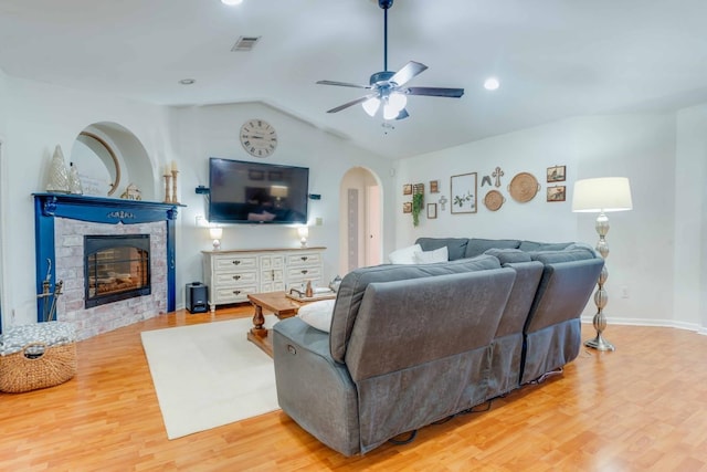 living room featuring a stone fireplace, lofted ceiling, ceiling fan, and light hardwood / wood-style flooring