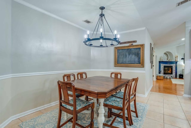 dining area featuring a stone fireplace, light tile patterned floors, an inviting chandelier, and ornamental molding