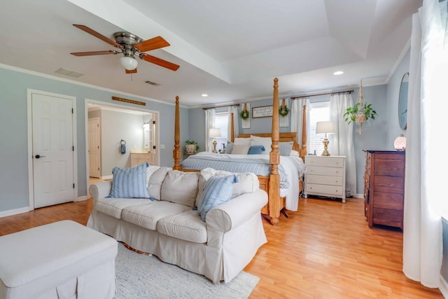 bedroom with light hardwood / wood-style floors, connected bathroom, ceiling fan, crown molding, and a tray ceiling