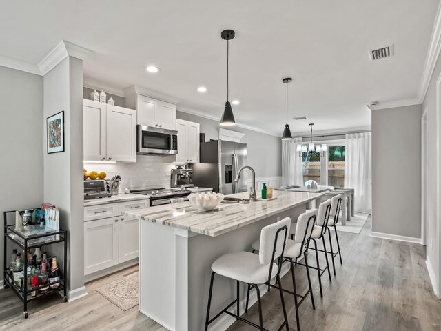 kitchen with white cabinetry, hanging light fixtures, an island with sink, and stainless steel appliances