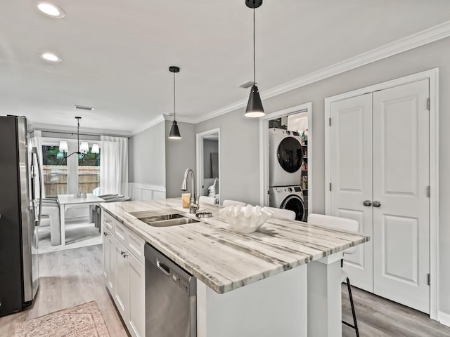 kitchen featuring stacked washing maching and dryer, stainless steel appliances, sink, white cabinets, and an island with sink