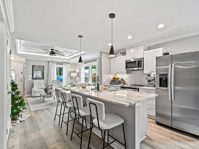 kitchen featuring pendant lighting, white cabinets, light stone countertops, an island with sink, and appliances with stainless steel finishes