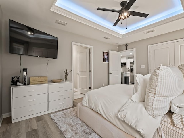 bedroom featuring light hardwood / wood-style flooring, a raised ceiling, and ceiling fan